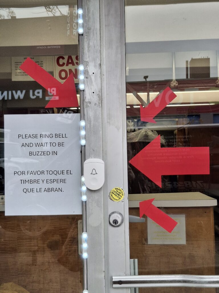 A door at a dry cleaners
There is a sign that says PLEASE RING BELL AND WAIT TO BE BUZZED IN / POR FAVOR TOQUE EL TIMBRE Y ESPERE QUE LE ABRAN

there are four large red arrows pointing directly at the bell